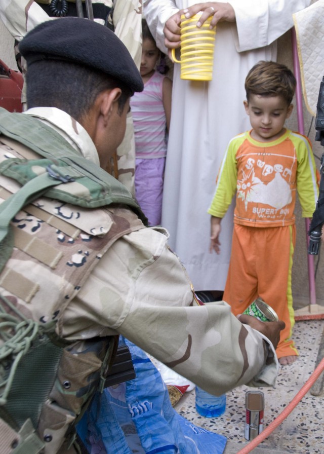 BAGHDAD - An Iraqi soldier from the 24th Brigade, 6th Iraqi Army Division distributes the contents of a food bag to residents of the "1st of June" area of Abu Ghraib during a joint Coalition Forces foot patrol on June 25. The joint patrols are design...