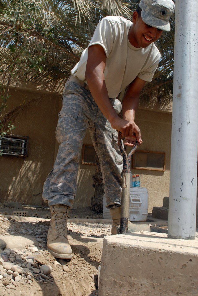 VICTORY BASE COMPLEX, Iraq - Spc. Michael Presentado, a native of Upper Marlboro, Md., assigned to E Company, 5th Battalion, 52nd Air Missile Defense Regiment, Multi-National Division - Baghdad, digs around the base of a flagpole here, June 26. "They...