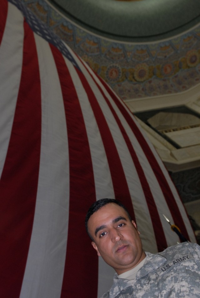 BAGHDAD - Iraqi-born U.S. Soldier turned American citizen, Spc. "Brown," an interpreter attached to the 225th Engineer Brigade, stands in front of a giant American flag inside al-Faw Palace before a naturalization ceremony July 4. Brown, who uses...