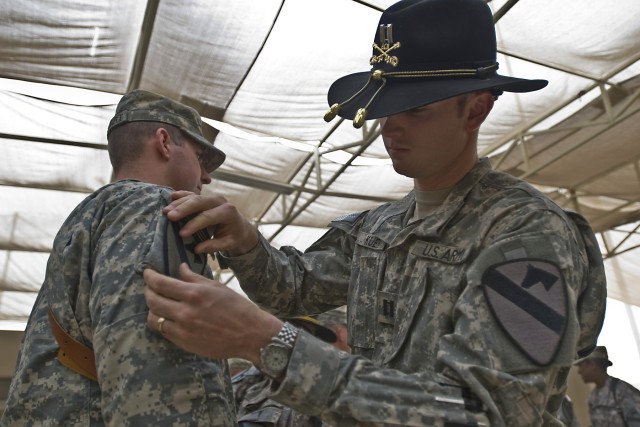 TAJI, Iraq - Capt. Andrew Kuen (right), of Montville, N.J., the commander of Headquarters and Headquarters Company, 1st Air Cavalry Brigade, 1st Cavalry Division, Multi-National Division - Baghdad, places a First Team combat patch on the shoulder...