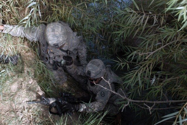 BAGHDAD -Sgt. 1st Class Matt Crouch, from Hudson, Mich., helps Staff Sgt. David Calangelo, from Vienna, W.V., cross an irrigation canal in the village of Arab Jasim here, July 3. Both Soldiers are assigned to A Troop, 1st Battalion, 150th Armor Recon...