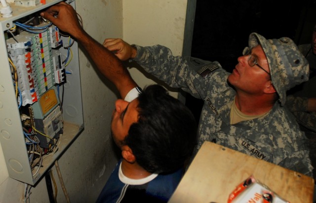 BAGHDAD -- Sgt. 1st Class John Pollard, of Fremont, N.C., helps a contractor fix electrical connections in a circuit breaker box at Joint Security Station Saydiyah, just south of Baghdad, July 1. Pollard is a platoon sergeant with Company B, 252nd Co...
