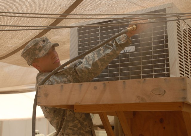 TAJI, Iraq - Spc. Brandon Harper of Pittsburgh, with 1st Platoon, 656th Signal Company, 56th Stryker Brigade Combat Team, blows dust out of an air conditioning unit July 10 at Camp Taji, Iraq, a base camp north of Baghdad. The unit cools a joint netw...