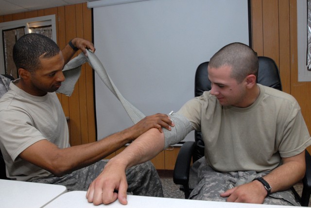 BAGHDAD - Sgt. 1st Class Eric Shaw of Mobile, Ala., carefully wraps an emergency trauma bandage around the upper arm of Pfc. Derek Romano, who hails from Salisbury, Md., during Individual First Aid Kit (IFAK) refresher class here, July 16. Both Soldi...