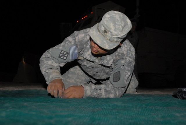BAGHDAD - Spc. Ivan Reyes, a native of Waco, Texas, carpenter with the 277th Engineer Company, 46th Engineer Combat Battalion (Heavy), 225th Engineer Brigade, weaves ties through sniper screen fabric into a chain linked fence during night operations ...