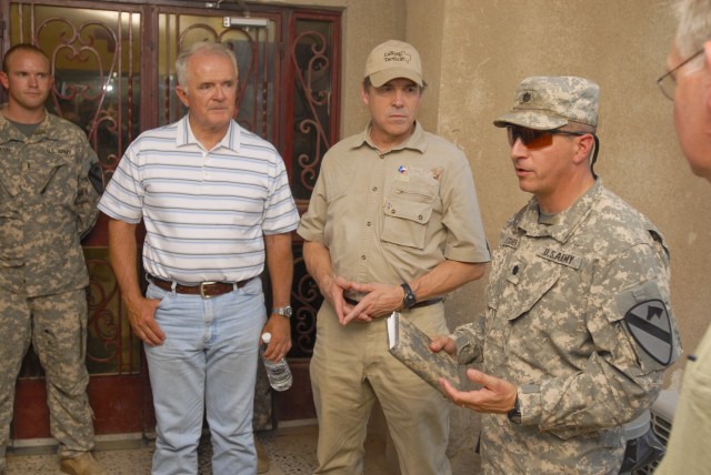 TAJI, Iraq- Nevada Gov. Jim Gibbons (left) and Texas Gov. Rick Perry (center), listen as Lt. Col. Ralph Litscher (right), from Half Moon Bay, Calif., commander of 2nd Battalion, 227th Aviation Regiment, 1st Air Cavalry Brigade, 1st Cavalry...
