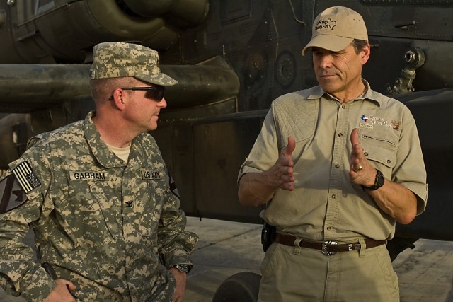 TAJI, Iraq- While standing in front of an AH-64D Apache attack helicopter, Texas Gov. Rick Perry (right) discusses weapons systems with Col. Douglas Gabram of Cleveland, Ohio, commander of the 1st Air Cavalry Brigade, 1st Cavalry Division,...