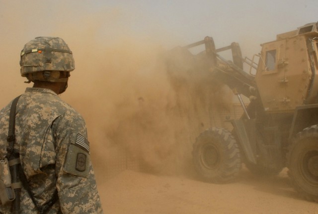 BAGHDAD - Pfc. Allen Gibson of Waco, Texas watches carefully as heavy equipment operator, Cpl. Charles Ham of St. Claire, Mo., dumps a load of dirt into a Hesco, July 22. The seven by seven by seven feet containers hold fill material that provides fo...