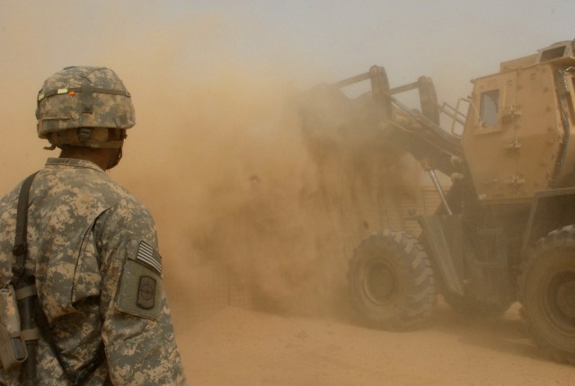 BAGHDAD - Pfc. Allen Gibson of Waco, Texas watches carefully as heavy equipment operator, Cpl. Charles Ham of St. Claire, Mo., dumps a load of dirt into a Hesco, July 22. The seven by seven by seven feet containers hold fill material that provides...