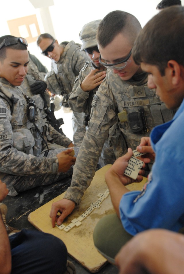 BAGHDAD - Staff Sgt. Jonathan Romero (left), a military police squad leader from San Antonio and Sgt. Bianca Leisure, an MP from Douglas, Ariz., look on as Pfc. Shane Venturi (right), a medic from Evansville, Ind., places his dominoes piece during a ...