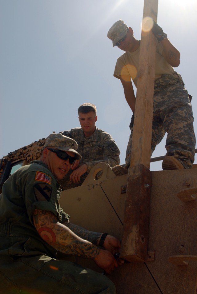 BAGHDAD - Sgt. Corey Elliott of Dekalb, Ill., Pfc. Cory Harding of Spokane, Wash., and Pfc. John Acosta of Victoria, Texas, install a wire mitigation kit on the top of a Mine-Resistant Ambush Protected vehicle in the Division Special Troops...