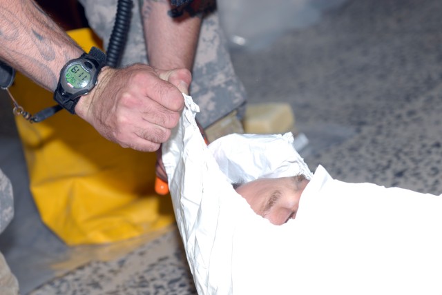 BAGHDAD - Staff Sgt Gregory Lowe uses a blade to cut away the hood of a compromised contamination suit from Sgt. Michael Kuca, demonstrating the proper way to remove a hazardous materials suit once the suit has been contaminated. Lowe is a...