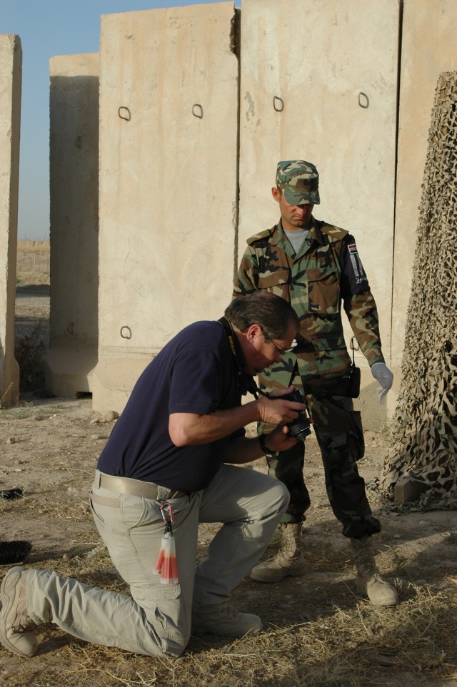 Carl Jonkers, an adviser with the Civilian Police Transition Team, teaches an Iraqi police officer how to take pictures of a crime scene. U.S. military forces and State Department advisors began an Iraqi Police "train the trainer" program in July on ...