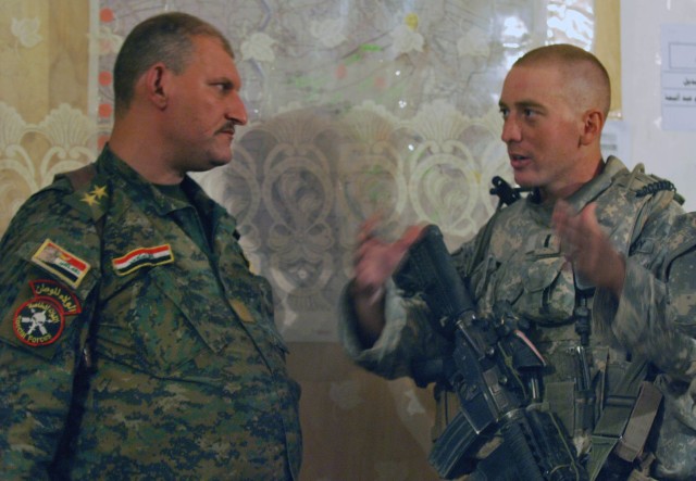 SALMAN PAK, Iraq - First Lt. Jeffrey W. Wismann (right), of Winchester, Ky., discusses upcoming operations with an Iraqi officer in the town of Salman Pak following a foot patrol July 30 in the Ma'dain region, located outside of southeastern Baghdad....
