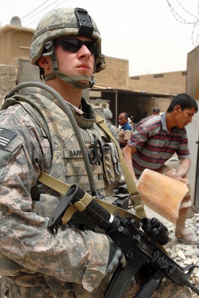 BAGHDAD - Spc. Steve 'Doc' Barrett, a combat medic from Vero Beach, Fla., assigned to 1st Squadron, 7th Cavalry Regiment, 1st Brigade Combat Team, 1st Cav. Division, guards the entrance to a tile-making factory as an employee dumps refuse onto a pile...