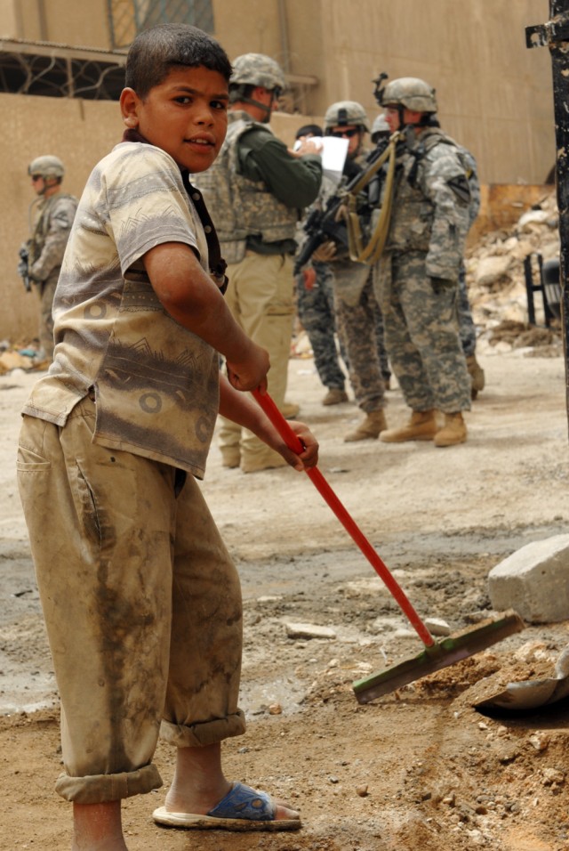 BAGHDAD – An Iraqi boy sweeps water and dirt away from the factory while members of the embedded provincial reconstruction team, civil affairs and cavalry scouts discuss the factory’s potential at stimulating the economy during a joint patrol with Ir...