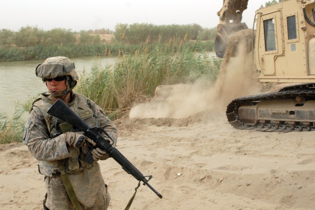 BAGHDAD - Spc. Shane Brassell, an Army Reserve Soldier from Whitney, Texas, and a heavy equipment operator assigned to the 277th Engineer Company, 46th Eng. Bn., 225th Eng. Bde., provides security and ground guides his fellow engineer near the river ...