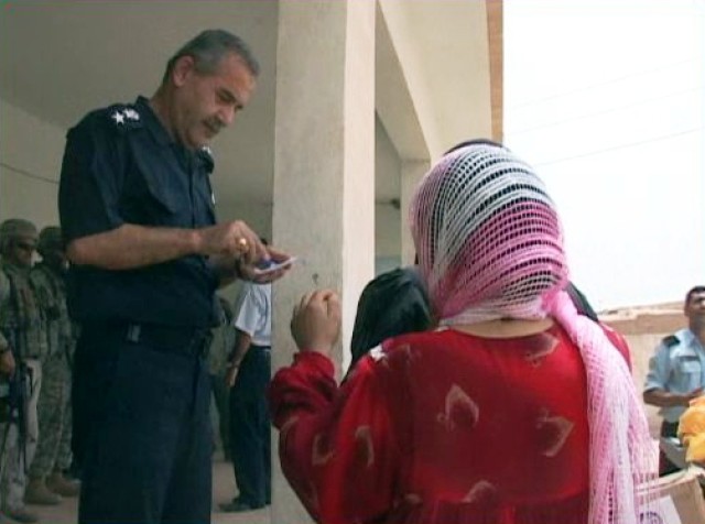 Lt. Col. Afram Jacob Jaji, the chief of the Arafa sub-district police station, in Kirkuk, Iraq, looks over an Iraqi woman's identification during a humanitarian aid delivery July 26. The IP with assistance from the U.S. Army delivered food, toys, and...