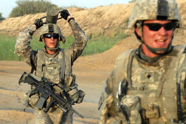 BAGHDAD - Spc. Johnathan Thompson (left), a cavalry scout from Lubbock, Texas, carries a post driver after setting up concertina wire barriers as Spc. Blake "Doc" Kent (right), a combat medic from Sugarland, Texas, communicates with a fellow Soldier ...
