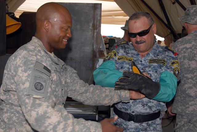 BAGHDAD - Warrant Officer Donnie Gray, of Houston, an allied trades technician, helps Maj. Gen. Abd al-Karim, commander of Rusafa Area Command, put on welder gloves before demonstrating for Karim how to weld armor to a pickup truck to be used by Iraq...