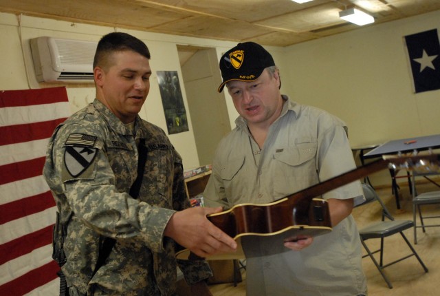 BAGHDAD - Killeen, Texas native, Maj. Brandon Reeves (left), brigade planner for 1st Brigade Combat Team, 1st Cavalry Division, hands a guitar to country music star Mark Chesnutt during a visit to Joint Security Station War Eagle Aug. 14.  The...