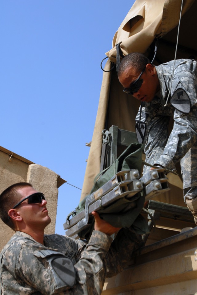 CAMP TAJI, Iraq - Greenville, S.C. native, Spc. Tavares Harris (right), a supply specialist, hands a cot to Killeen, Texas native, Pfc. Timothy Dobelbower, an artillery cannon crewmember, both assigned to Battery A, 1st "Dragon" Battalion, 82nd...