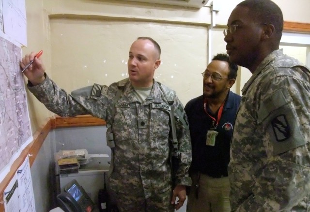 During a July 24 planning meeting, Lt. Col. William B. Smith, Jr. (left), COL Q-West Mayor, outlines a mission to catalog valve boxes and major taps on the Q-West water pipeline to Reinaldo Guebara (middle), a civilian contractor and Capt. James...