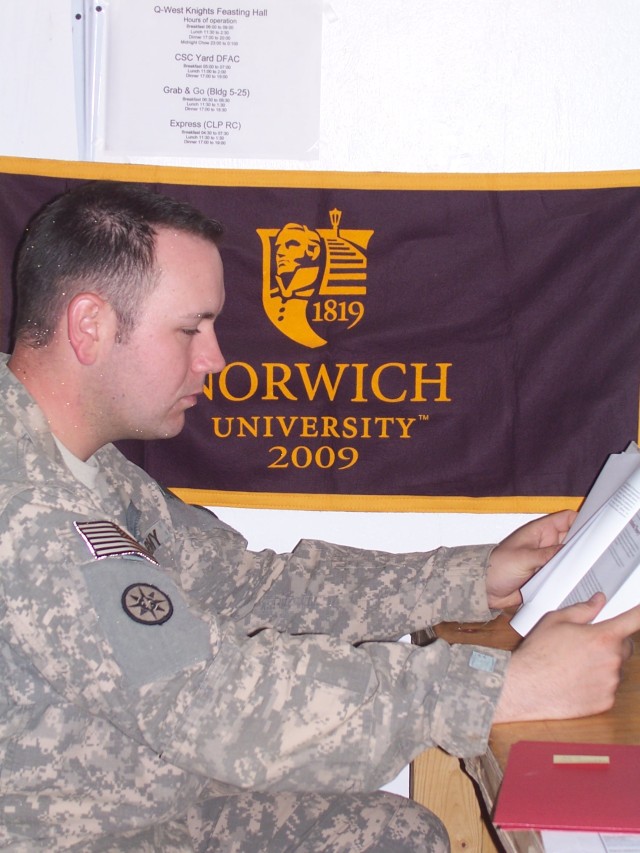 Spc. Christopher Brown, an administrative assistant with the 395th Combat Sustainment Support Battalion, cracks open some study materials at his desk, where he proudly displays a Norwich University flag, his alma mater. Brown, from Ashland, Mass., is...