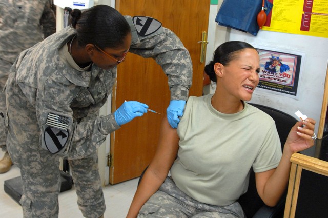 BAGHDAD - Staff Sgt. Renatta Draper (right), from Bemidji, Minn., winces as Sgt. Danielle Dubose, a health care non-commissioned officer, from Detroit, gives her the annual flu shot at the Battalion Aid Station, on Camp Liberty, Oct. 1.  All personne...