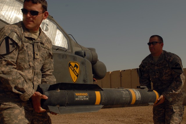 CAMP TAJI, Iraq - Spc. Scott Shaver, of Austin, Texas (left) and Spc. Bret Gibson, of Wichita, Kan., haul a Hellfire missile to load onto the mounting bracket of an AH-64D Apache helicopter, here, Oct. 1. Both Soldiers are armament electrical...