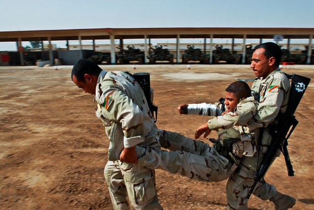 CAMP TAJI, Iraq-During first aid training two  Iraqi Soldiers carry a wounded comrade to safety after treating his wounds, here,  Oct.12. The training helps to sustain previous first aid skills and teach newer IA Soldiers how to respond in an emergen...