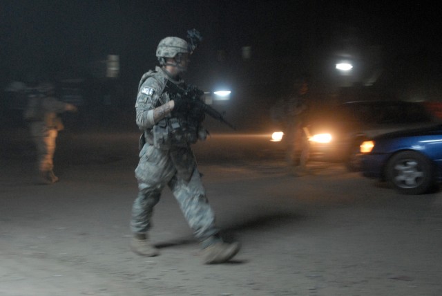 BAGHDAD - As cars pass by in eastern Baghdad, Oct. 18, Sgt. Ryan Tullis (center), a forward observer from Gillette, Wyo., assigned to Company C, 2nd Battalion, 5th Cavalry Regiment, 1st Brigade Combat Team, 1st Cavalry Division, patrols with IA...