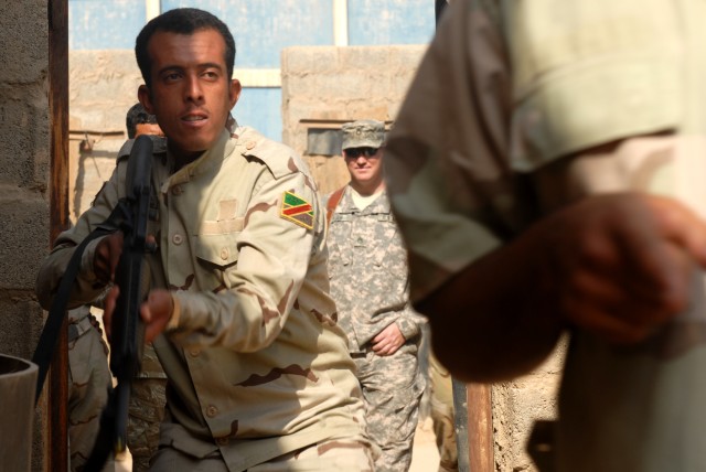 BAGHDAD - An Iraqi Army Soldier enters through a doorway in order to clear a room during a training exercise for an academy held at Joint Security Station Shield, here, Oct. 19. Staff Sgt. Kirk High (background), from Fort Worth, Texas, an...