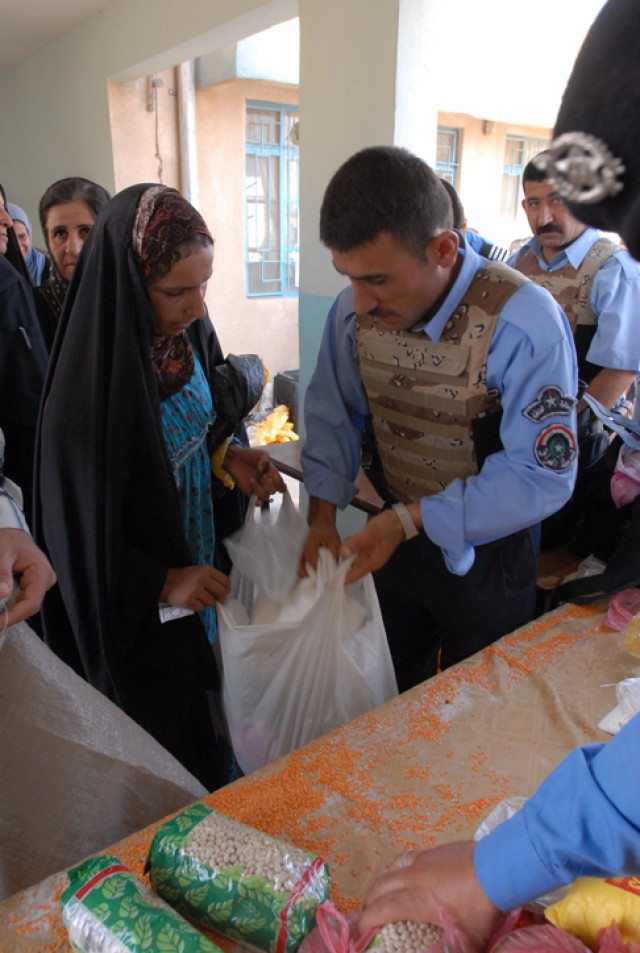 An Iraqi policeman gives out food to a woman during a humanitarian aid delivery in the Nasser neighborhood of Kirkuk city, Iraq, Oct. 24. This aid drop was an opportunity for people within the community to see the IP working together with U.S....