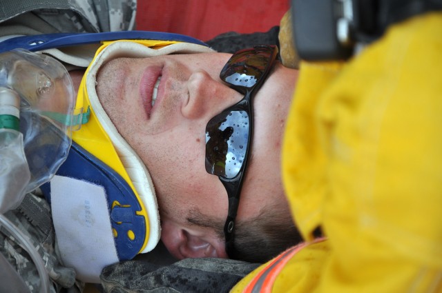 Role player Sgt. Josh Tharpe, a tank crewmember with C Company, 2nd Battalion 198th Combined Arms Brigade and Grenada, Miss., native, watches as Q-West firefighters examine him during a mass casualty exercise here Oct. 28. (U.S. Army photo by Sgt....