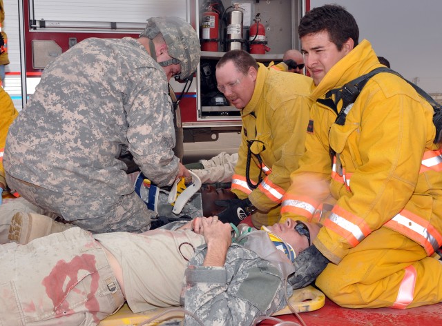 Q-West firefighters Chas Cosgrave (right), a Zanesille, Oh., native and Michael Winter, a Salt Lake City native, take care of role playing patient, Sgt. Josh Tharpe, a tank crewmember with C Company, 2nd Battalion 198th Combined Arms Brigade and Gren...