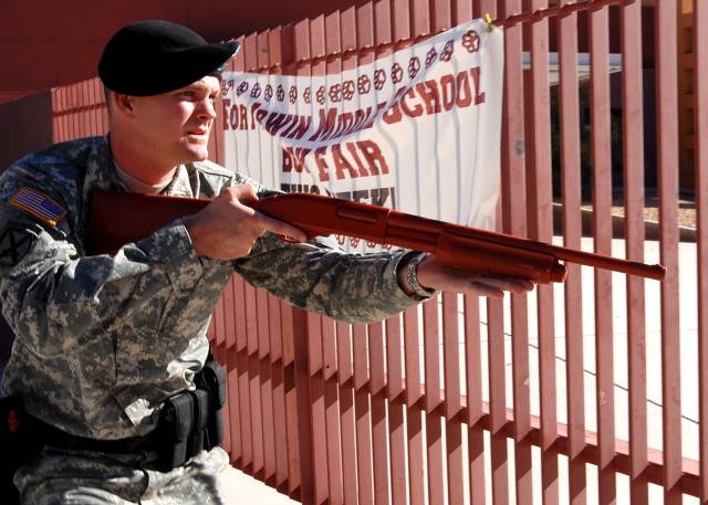 Sgt. Benjamin Robinson, a team leader military police officer with the Fort Irwin U.S. Army Garrison Military Police Company, approaches an entrance to Fort Irwin Middle School with a "dummy" shotgun during a training event Oct. 25. The scenario invo...