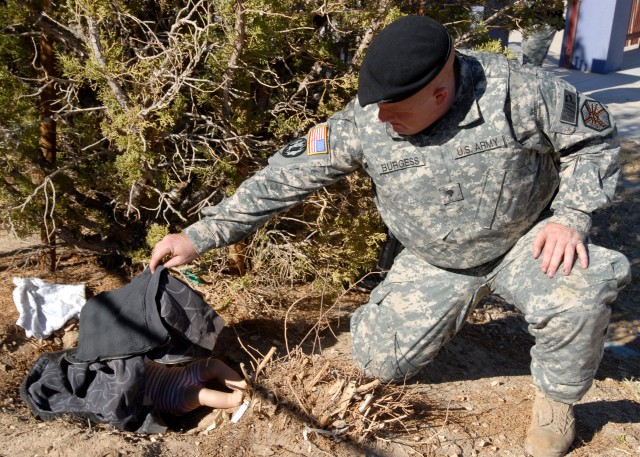 Spc. Christopher Burgess, a military police officer with the Fort Irwin U.S. Army Garrison Military Police Company, uncovers a doll mimicking the body of a dead baby during a training event Oct. 24 at Fort Irwin Middle School. The "crime scene" provi...