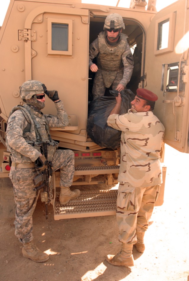An Iraqi Army soldier receives school supplies from a U.S. Army Soldier with 4th Squadron, 9th Cavalry Regiment, 2nd Brigade Combat Team, 1st Cavalry Division, during a school supply drop in the village of Abu Shahab in Kirkuk province, Iraq, Nov....