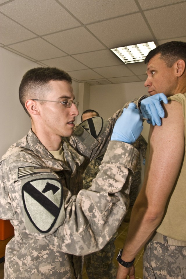 CAMP LIBERTY - Spc. Justin Roberts (left) gives an H1N1 flu shot to Master Sgt. Tim Metcalf, of Cedar Fort, Utah, here, Nov. 23. Roberts, a native of Galveston, Texas, is a medic assigned to the Disivion Special Troops Battalion Aid Station....