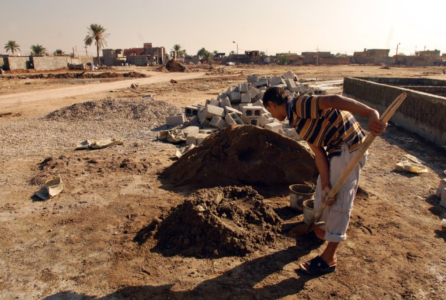 A Taza, Iraq, resident loads cement with a shovel to help a neighbor rebuild his home, one bucket at a time, following a devastating car-bomb attack which killed approximately 90 residents and wounded more than 200 in Taza last June....