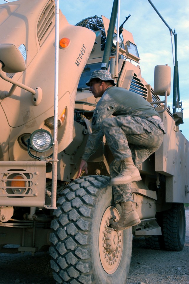 CONTINGENCY OPERATING LOCATION Q-WEST, Iraq - Pfc. William C. Williamson, a native of Seattle, Wash., and vehicle turret gunner, jumps up to examine the engine of his Mine-Resistant, Ambush-Protected vehicle at the Convoy Readiness Center yard at...