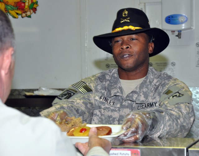 Sgt. 1st Class Aaron Finley, 15th Sustainment Brigade schools and training noncommissioned officer, serves Thanksgiving dinner in the dining facility here, Nov. 26. It is traditional for senior noncommissioned officers and commissioned officers to...