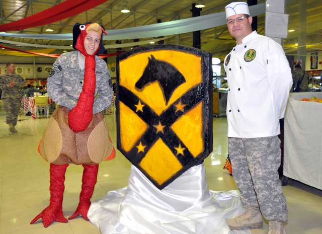 Spc. Carlos Seijo [left], a 15th Sust. Bde. cook, dresses like a turkey while Pfc. Daniel Rivera, also a 15th cook, stands by the hardened sugar "Wagonmaster" patch he created during a Thanksgiving feast here, Nov. 26. (U.S. Army photo by Sgt....