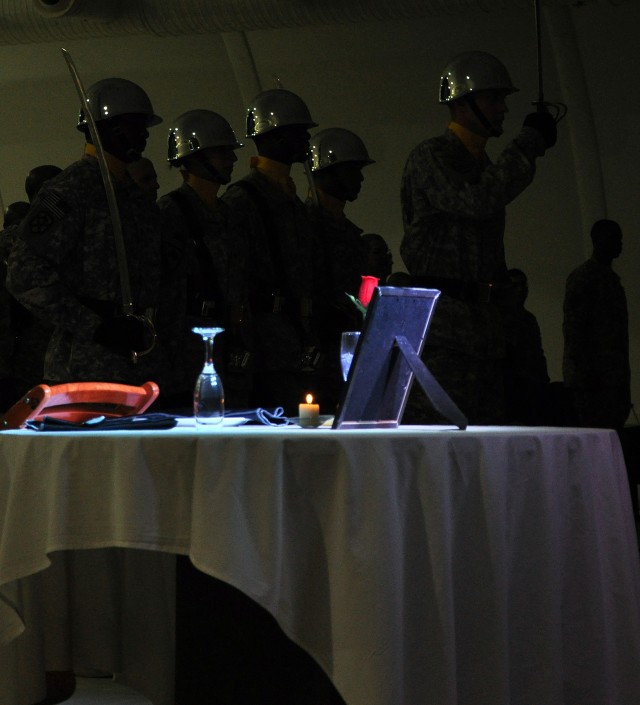 Soldiers of the 15th Special Troops Battalion color guard prepare to remove the colors behind the Fallen Soldier's Table, which memorializes Soldiers missing or killed in action and prisoners of war, at an NCO induction ceremony in the Morale...