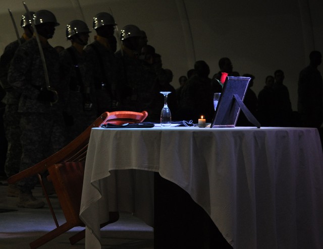 Soldiers of the 15th Special Troops Battalion color guard prepare to remove the colors behind the Fallen Soldier's Table, which memorializes Soldiers missing or killed in action and prisoners of war, at an NCO induction ceremony in the Morale...