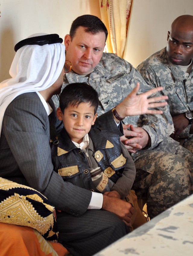 One of Shaykh Doctor Mohammad's children sits in his lap while he speaks with Col. Larry Phelps, 15th Sust. Bde. commander and Greenville, Ala., native, during a visit here by 15th Sust. Bde. leaders Dec. 16. (U.S. Army photo by Sgt. Matthew C. Coole...