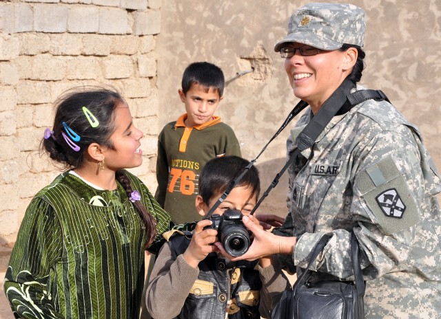 A local boy takes pictures with Master Sgt. Celia Feller, night operations noncommissioned officer in charge for 15th Sust. Bde. and Farmington, N.M., native, who jokingly wears a major's hat during a visit here by 15th Sust. Bde. leaders Dec. 16. (U...