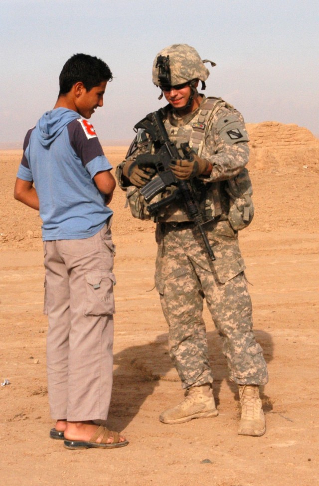 CONTINGENCY OPERATING LOCATION Q-WEST, Iraq - Sgt. Patrick A. Martin (right), a truck commander from Southaven, Miss., chats with an Iraqi boy outside the village of Ejbah who greeted the Soldiers during a presence patrol Dec. 15. Martin serves...