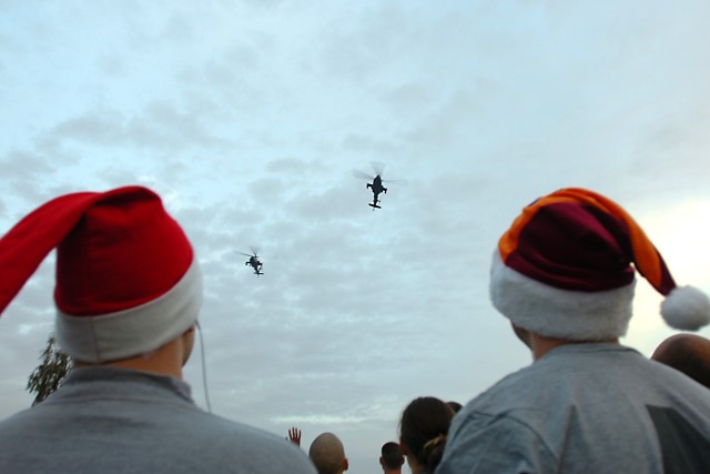 CAMP TAJI, Iraq - Two Soldiers watch as a pair of AH-64D Apache attack helicopters from 4th Battalion, 227th Aviation Regiment, 1st Air Cavalry Brigade, 1st Cavalry Division, perform a low flyover for runners before the kick-off of the 5K Jingle...